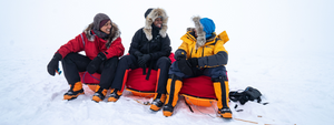 3 women sitting in the snow wearing cold-weather apparel layers