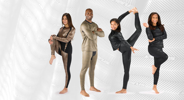 far left woman standing holding one knee up in front in body mapped base layer top and bottom in rose gold middle left man standing arms crossed in winter weight base layer in coyote middle right woman in dynamic stretch weather winter weight base layer in carbon far right woman standing with one leg raised in all season base layer in carbon